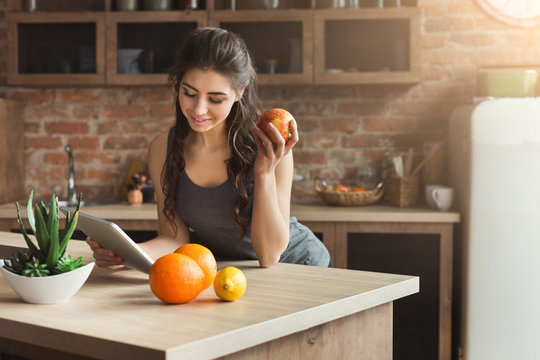 Happy young woman eating fruits in kitchen
