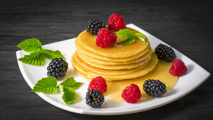 pancakes with honey raspberries and blackberries on a black wooden background