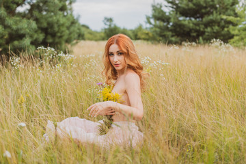 Fototapeta na wymiar Natural beauty. Sexy fashion portrait of nice young red hair woman sitting on meadow, facing the sunset. Woman with pretty face in green field with red poppy flowers outdoor 