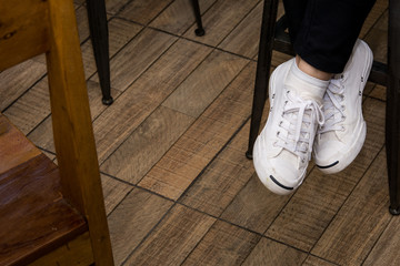 Detail of canvas shoes of a woman sitting cross legs on a high stool in cafe, Wooden floor background