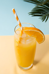 Glass of fresh orange juice and green palm leaves on pastel background. Pop art design, minimal summer concept.