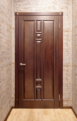 Brown metal with wooden overlays entrance door with brass handle in corridor with floor tiled in beige