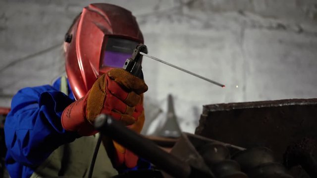 cute welder girl in uniform in the garage working with welding equipment. Women's work in art