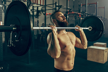 Fototapeta na wymiar Fit young man lifting barbells working out in a gym