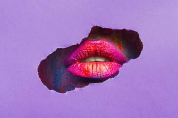 Red lips through torn slot of purple paper