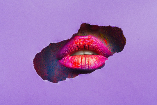 Red lips through torn slot of purple paper