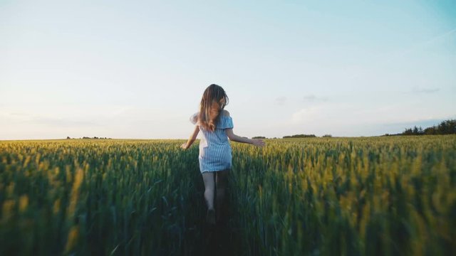 Happy girl in dress running in a green field of a young rape 4K