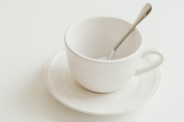 Obraz na płótnie Canvas Empty cup of white color and small spoon on white table. Minimal style
