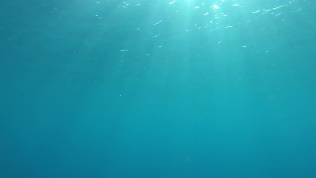 SLOW MOTION, UNDERWATER: Bright sunrays shining trough the tranquil crystal clear ocean surface near Tahiti. Beautiful shot of the turquoise sea water glistening in the warm tropical summer sunshine.