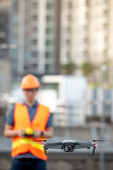 Young Asian engineer flying drone over construction site. Using unmanned aerial vehicle (UAV) for land and building site survey in civil engineering project.