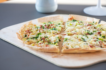 Original dünner Flammkuchen aus dem Elsass mit Zwiebeln, Speck und Sauerrahm Creme im Ofen gebacken uf einem Holzbrett serviert