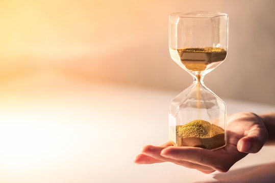 Close up of brown sand running through the shape of modern hourglass on male hand.Time passing and running out of time. Urgency countdown timer for business deadline concept with copy space