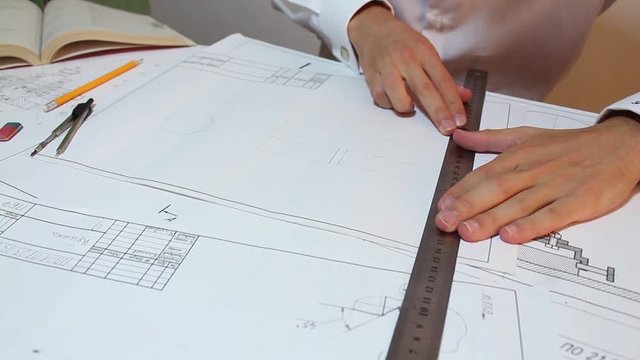 This stock video features a young male engineer at work, drawing at his office desk. Several drawing materials are spread across the table.