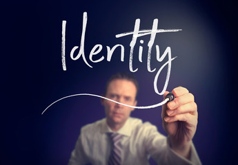 A businessman writing a identity concept with a white pen on a clear screen.