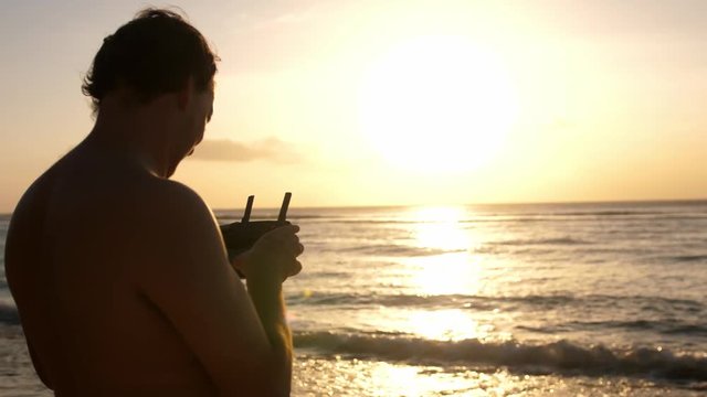 Man operating a drone with remote control. Quadro copter drone flying over sunset ocean. 3840x2160
