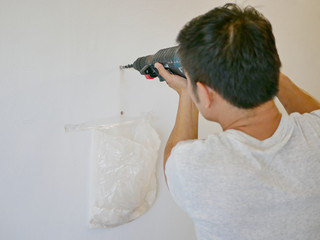 An electric drill being used by Asian handy man drilling into concrete wall