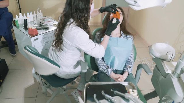 Slowly shooting the dentist in her office put a seal on the young girl to the patient and warms her with a photopolymerizer. The concept of dental treatment, seals, drill, people, health, beauty