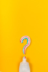 Colored toothpaste in form of question sign on yellow background top view