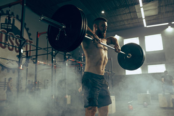 Fototapeta na wymiar Fit young man lifting barbells working out in a gym
