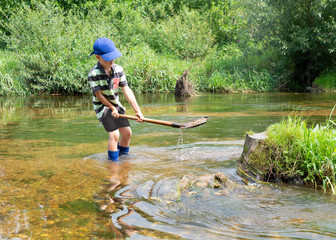 Schulkind spielt im Wasser mit einer Schaufel, Kind