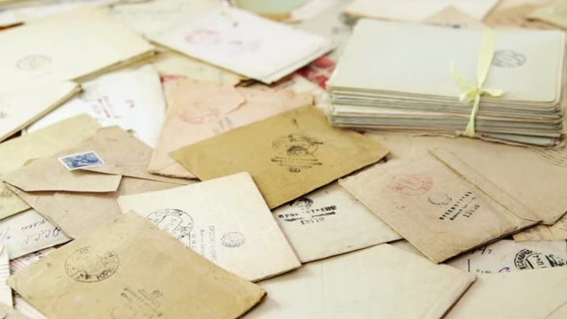Hands of an old woman sort through mail letters on the table. Envelopes are stamped: "Viewed by military censorship"