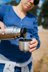 Naklejka premium Woman pouring hot tea from a thermos in the open air. On a sandy beach on a Sunny day. Close up.