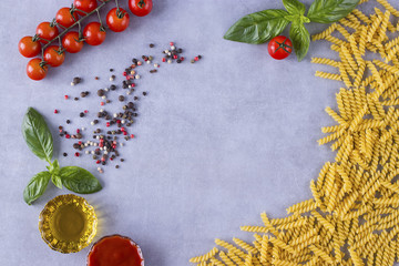 Pasta in the form of spiral, cherry, fresh basil, tomato paste and olive oil on gray concrete background.