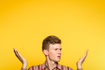 uncomprehending bewildered puzzled perplexed confused man pointing upwards with hands. portrait of a young guy on yellow background pop up or peek out from the bottom. free space for advertisement.