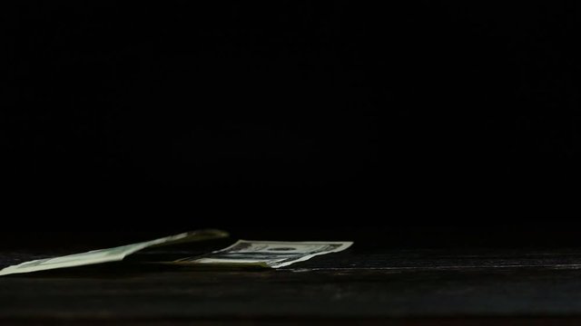 US dollar bills falling down,side view. 100 US dollar banknotes flipping down to old wooden table with  black background ,hd slow motion video.