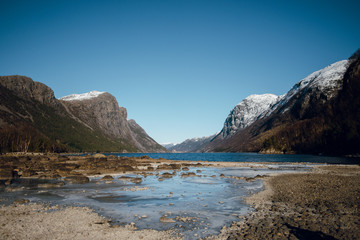 Beautiful view of rocky sea shore and beautiful mountains with snow peaks. Stony river bank. Sunny day in Fjord, Norway.