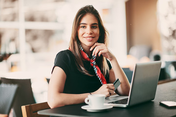 Happy young woman using credit card and laptop for shopping while sitting in cafe.