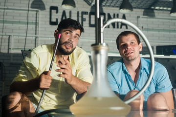 Friends men drink beer, smoke a hookah and have fun sitting