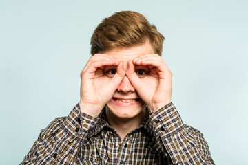 funny ludicrous joyful comic playful man pretending to look through binoculars. portrait of a young guy on light background. emotion facial expression. feelings and people reaction.
