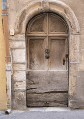 very old weathered brown arched door in ancient wall of medieval village in french provence