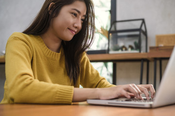 Young asian woman working with the laptop on a desk with her smile. Young woman working on weekend with her laptop in a warm sunlight day. Laptop working in the house concept.