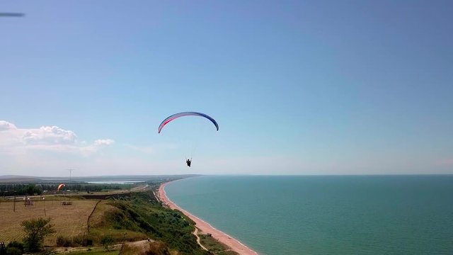Aerial View. The paraglider flies over the coastline. The wing of the paraglider is blown by the wind. Row of sea and forest