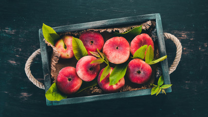 Flat peach in a wooden box. On a black wooden background. Top view. Free space for your text.