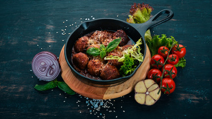 Meatballs with tomato sauce and vegetables in a frying pan. On a wooden table. Top view. Copy space.