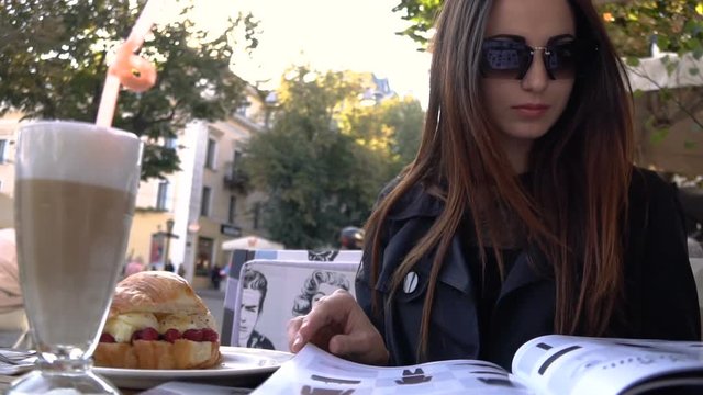 Attractive modern young woman drinks aromatic coffee in a cafe on a summer terrace and leaf over fashion magazine