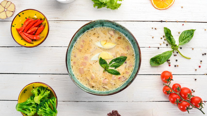 Creamy soup with bacon, chicken egg, vegetables and basil. On a wooden table. Top view. Copy space.