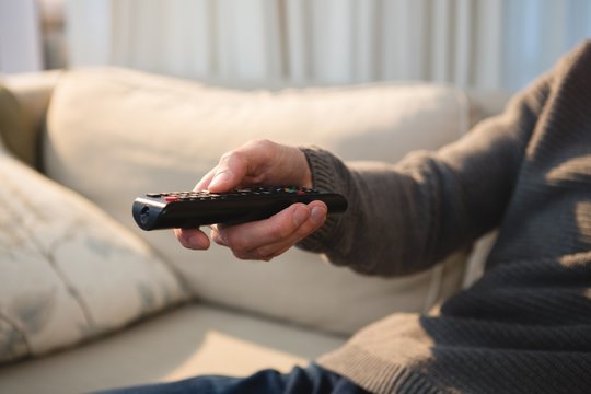 Man changing channel with remote control at home