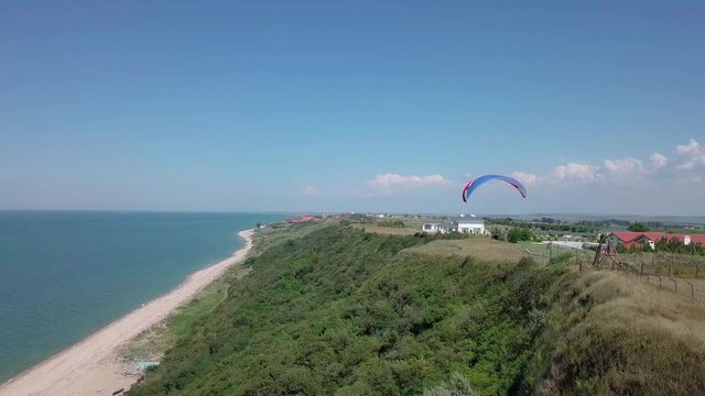Aerial View. The paraglider flies over the coastline. The wing of the paraglider is blown by the wind. Row of sea and forest