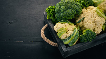 Cauliflower and broccoli in a wooden box. Fresh vegetables. On a wooden background. Top view. Copy...