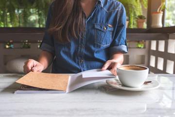 Closeup image of a woman opening a book with coffee cup on table in modern cafe