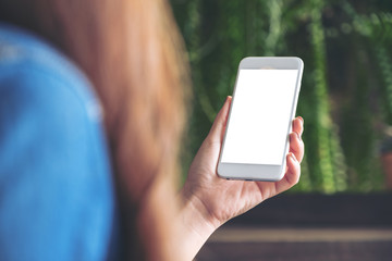Mockup image of a woman holding and looking at a white smart phone with blank desktop screen with blur green nature background