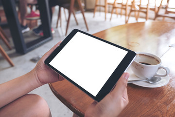 Mockup image of a woman sitting and holding black tablet pc with white blank screen with coffee cup on table