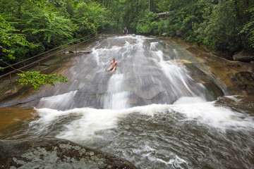 Tourists slide down a North Carolina waterfall. - obrazy, fototapety, plakaty