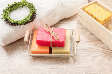 Three colorful soaps are placed in a basket, placed next to a towel on a wooden floor.