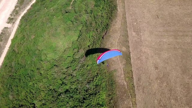 Aerial View. The paraglider flies over the coastline. The wing of the paraglider is blown by the wind. Row of sea and forest