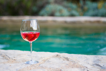Glass of Rose with strawberries next to swimming pool